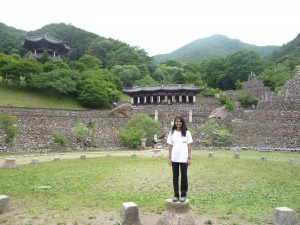 Aparna standing at a cultural site with mountains in the background