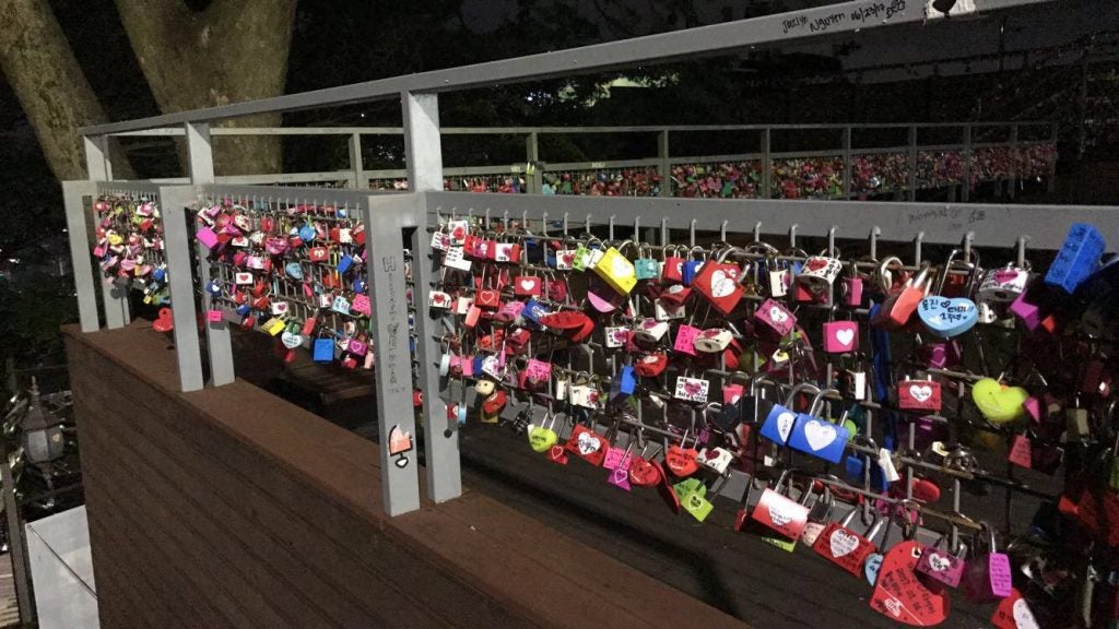 Many colorful locks hang from a metal fence