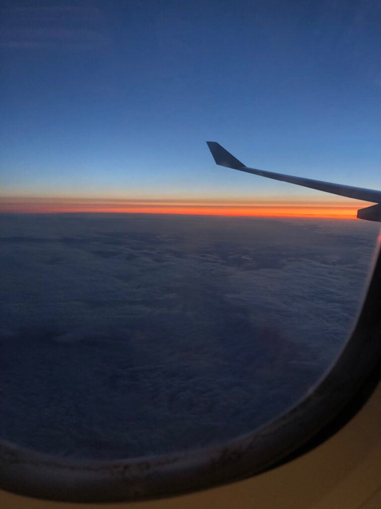 the wing of a plane is in view looking out the window during sunrise