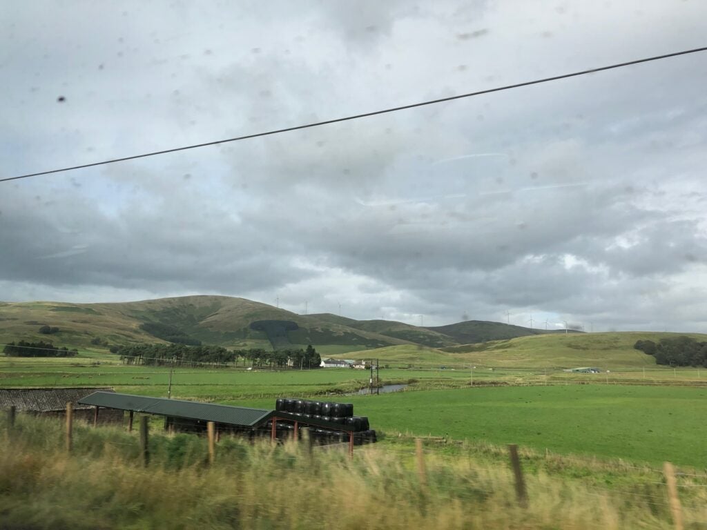 looking out at a greeb field on a cloudy day with a backdrop of mountains