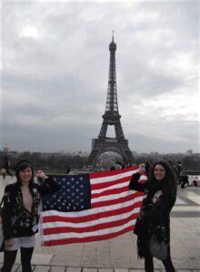 Two girls standing in front of Eiffel Tower holding United States flag.