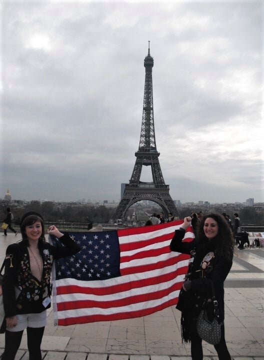 Two girls standing in front of Eiffel Tower holding United States flag.