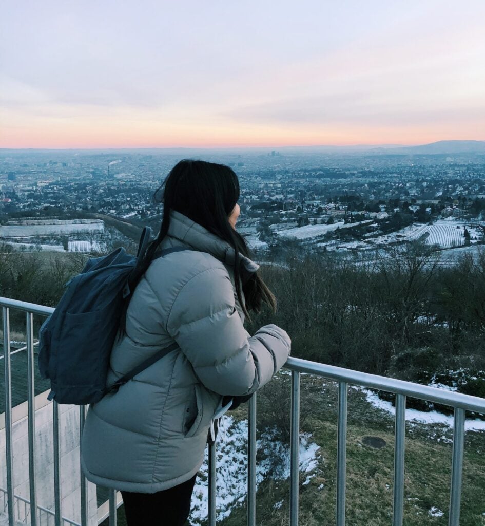 woman stands at railing overlooking city at sunset