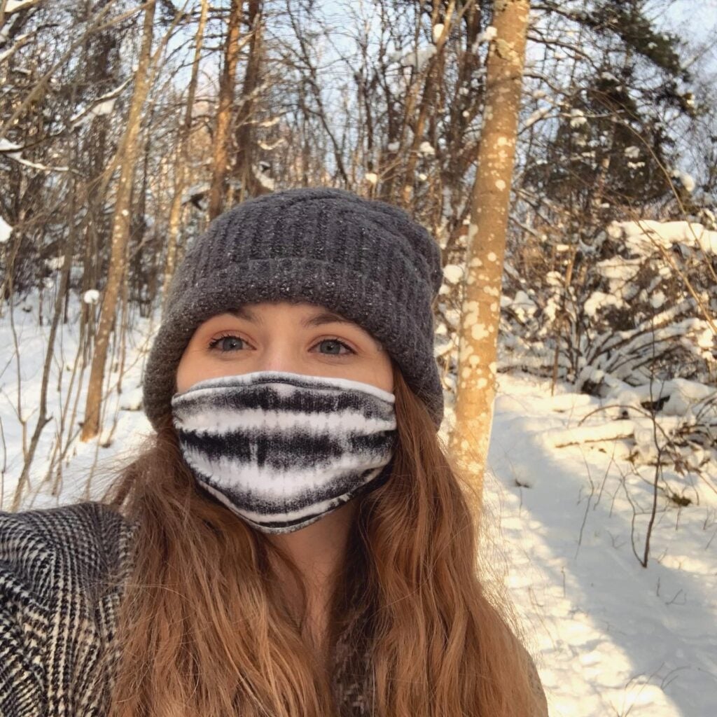 Girl wearing face mask and beanie near snow and trees during daytime