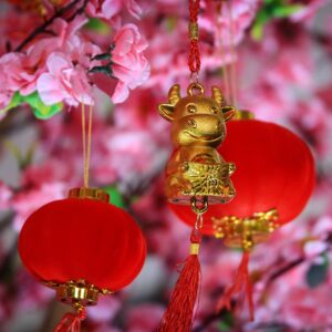 small golden ox decoration hangs near red and gold spherical decorations near pink flowers