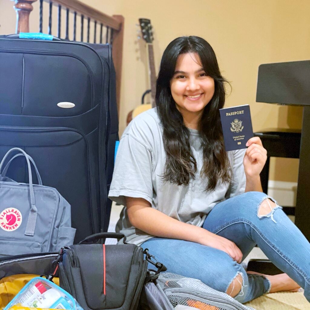 girl smiles holding up passport and sitting near many bags