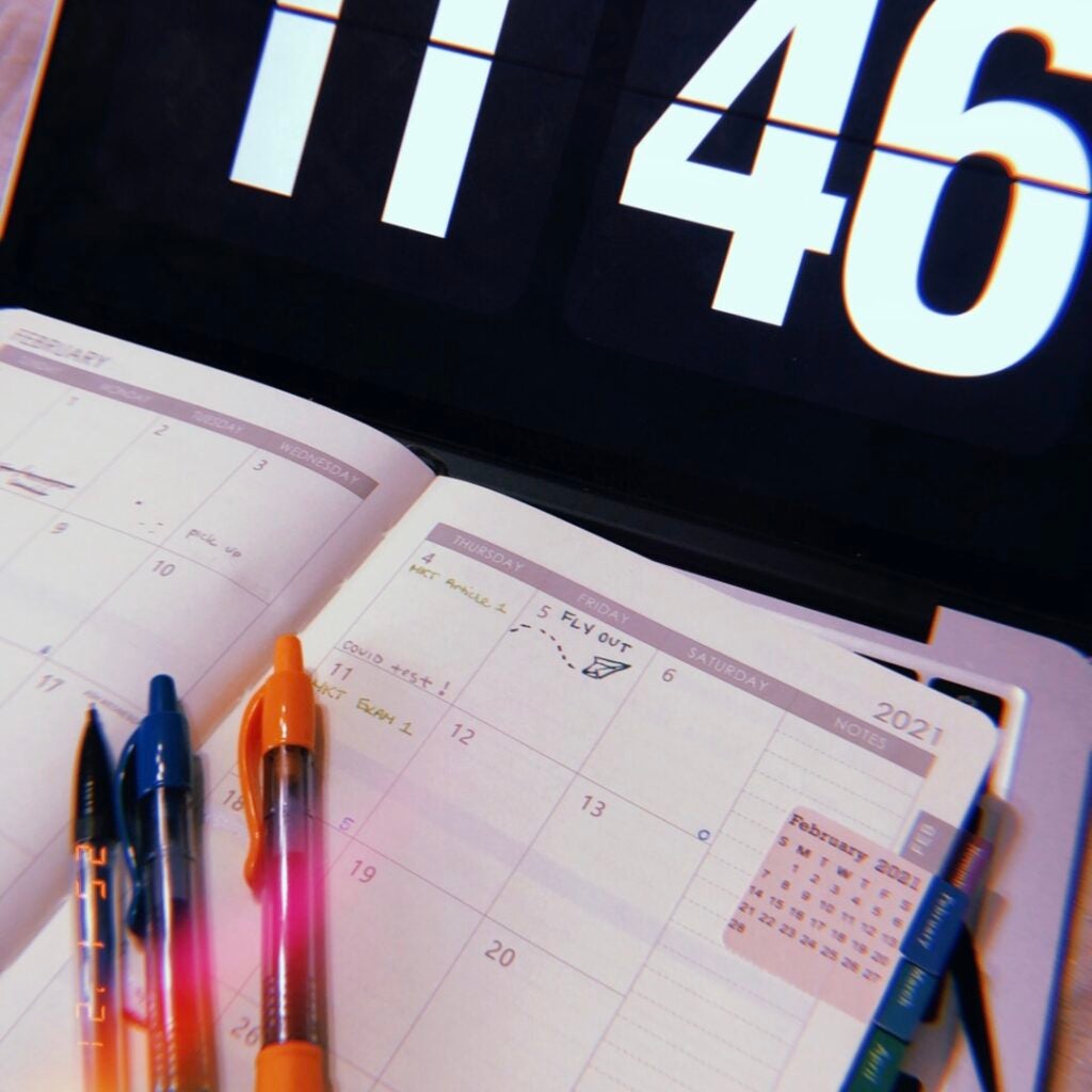 open planner with colourful pens and a clock