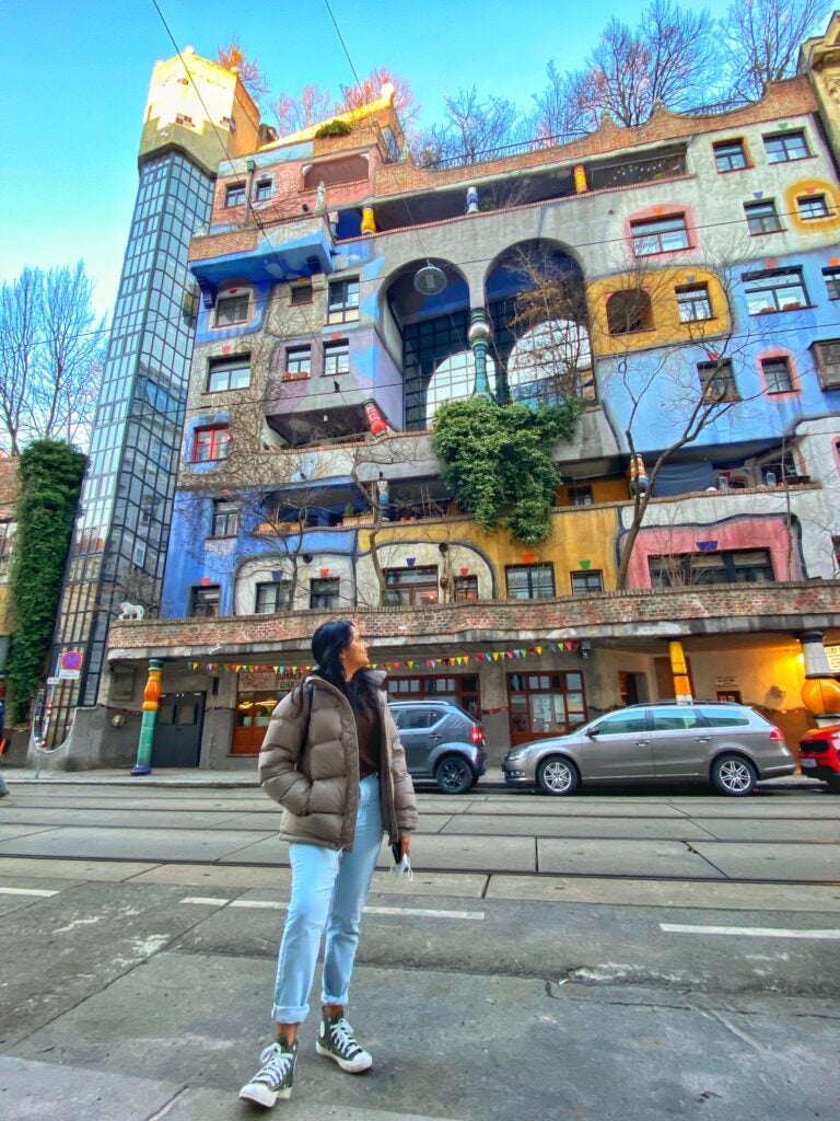 person stands in front of colourful buildings and street with cars during daytime