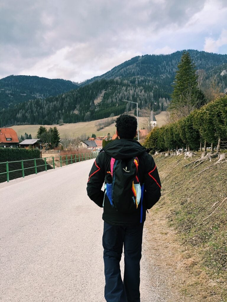 person wearing a backpack walks on trail near mountains during daytime