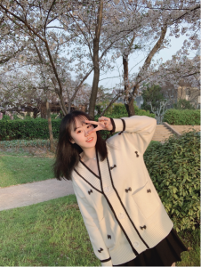 young woman stands near greenery and sidewalk during daytime