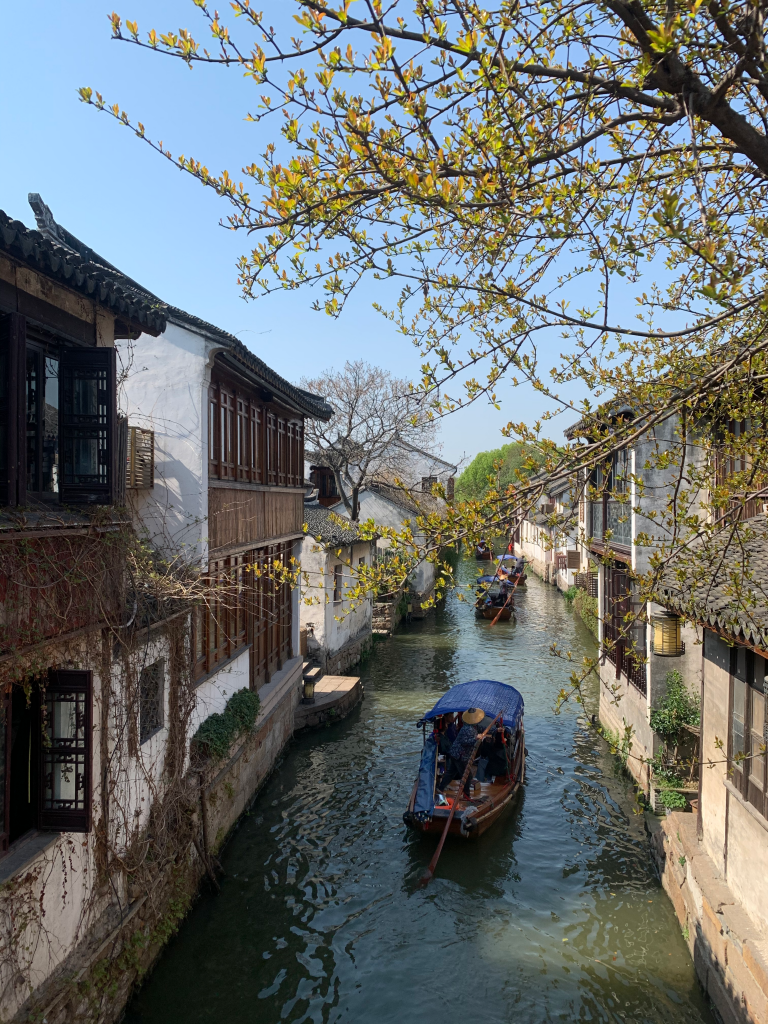 boat in canal banked by buildings near trees during daytime