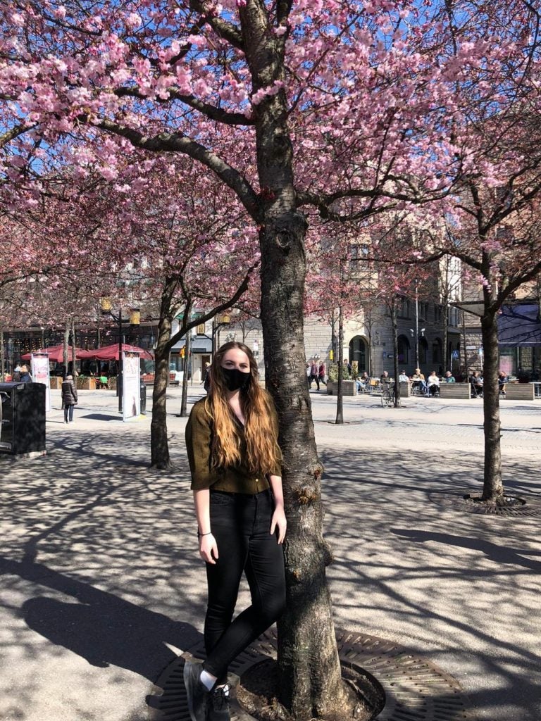 woman stands under flowering tree near buildings during daytime