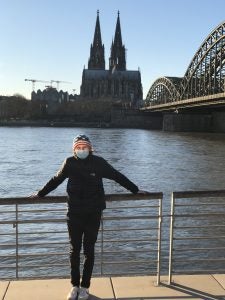 person wearing face mask stands near body of water and bridge with towers in background during daytime