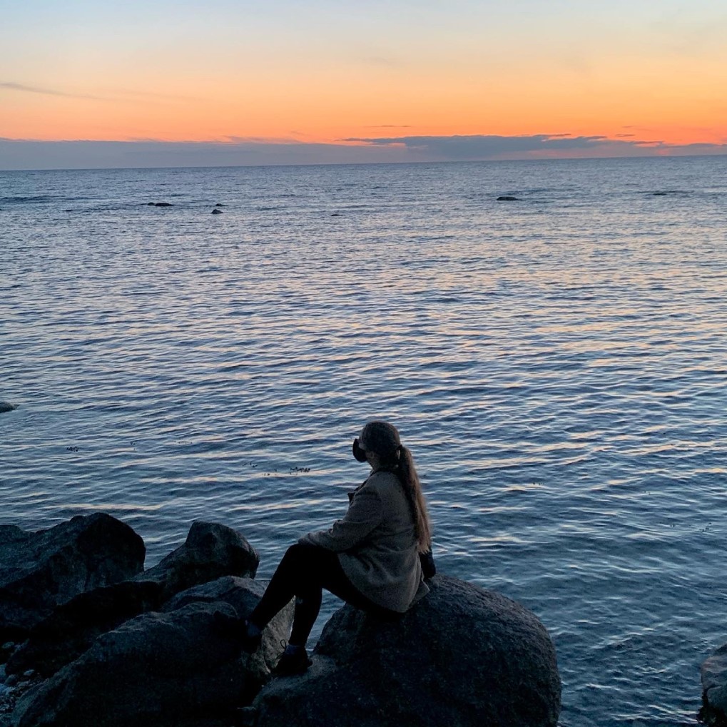woman sits on rocks near large body of water during sunset