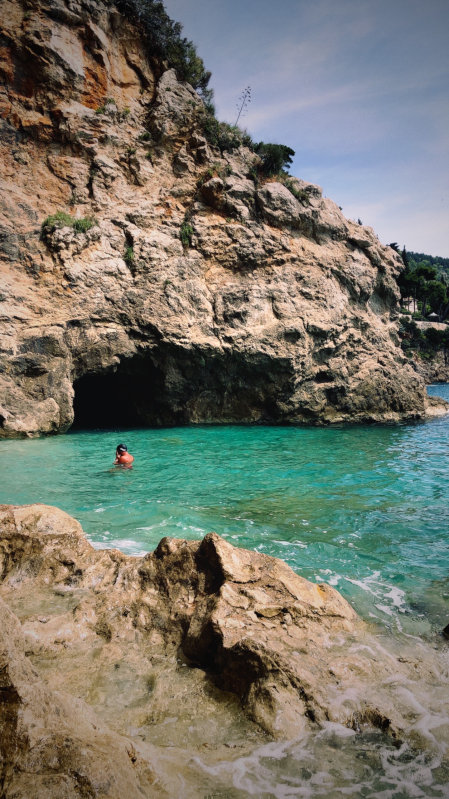 person swimming in clear waters near natural rock formation during daytime