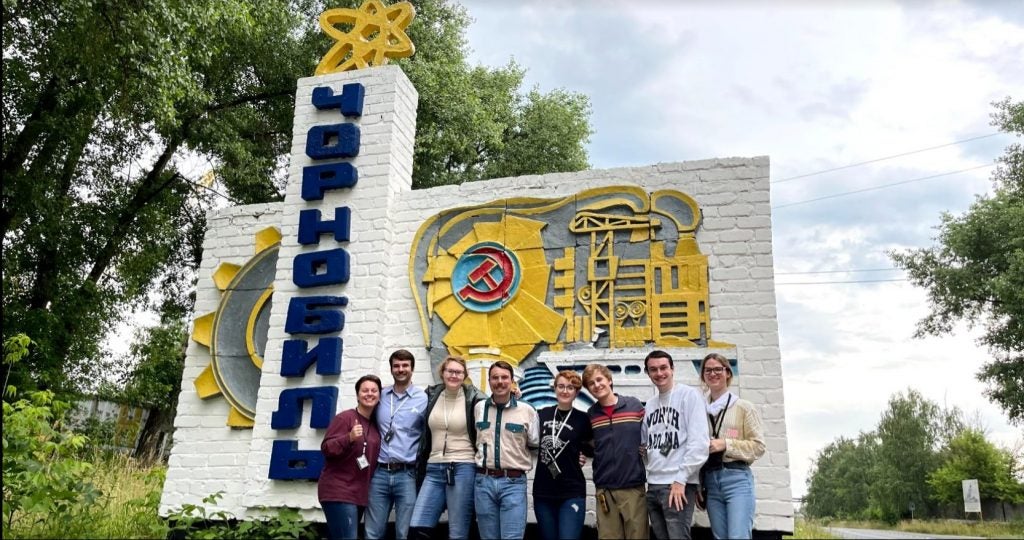 Kylie stands with a group of friends in front of a large stone sign.