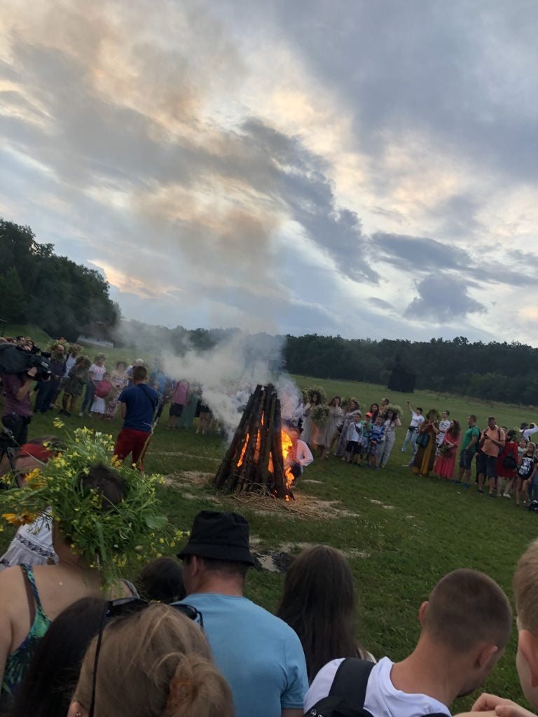 In an open field, people gather around bonfire preparations.