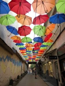 A village alley with colorful umbrellas hanging over-head.