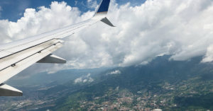 Birds-eye view from an airplane window of blue sky, white clouds and San Jose city below.