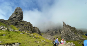 The Old Man of Storr, a unique rock formation on the Isle of Skye that is actually a massive, ancient landslide. Around the formation, a misty blue sky.