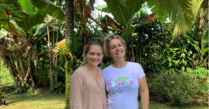 Makayla stands with her arm around her host mom, they both smile in front of leafy green trees. 