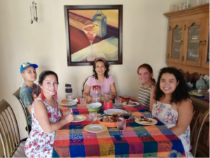 Makayla sits at a table with 4 friends, eating empanadas set on top of a colorful table cloth. 