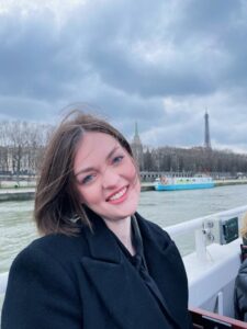 Eliza smiles on a boat. Behind her, you can see the water and city buildings in the distance