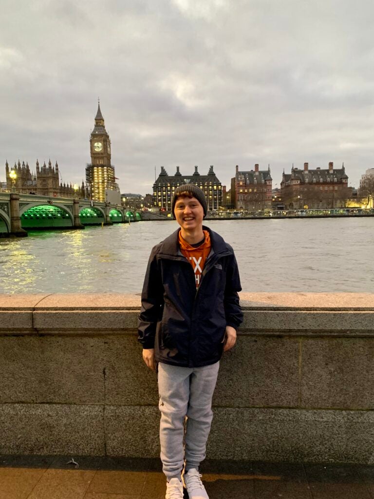 Devin smiles in front of the water with a view of Tower Bridge behind him