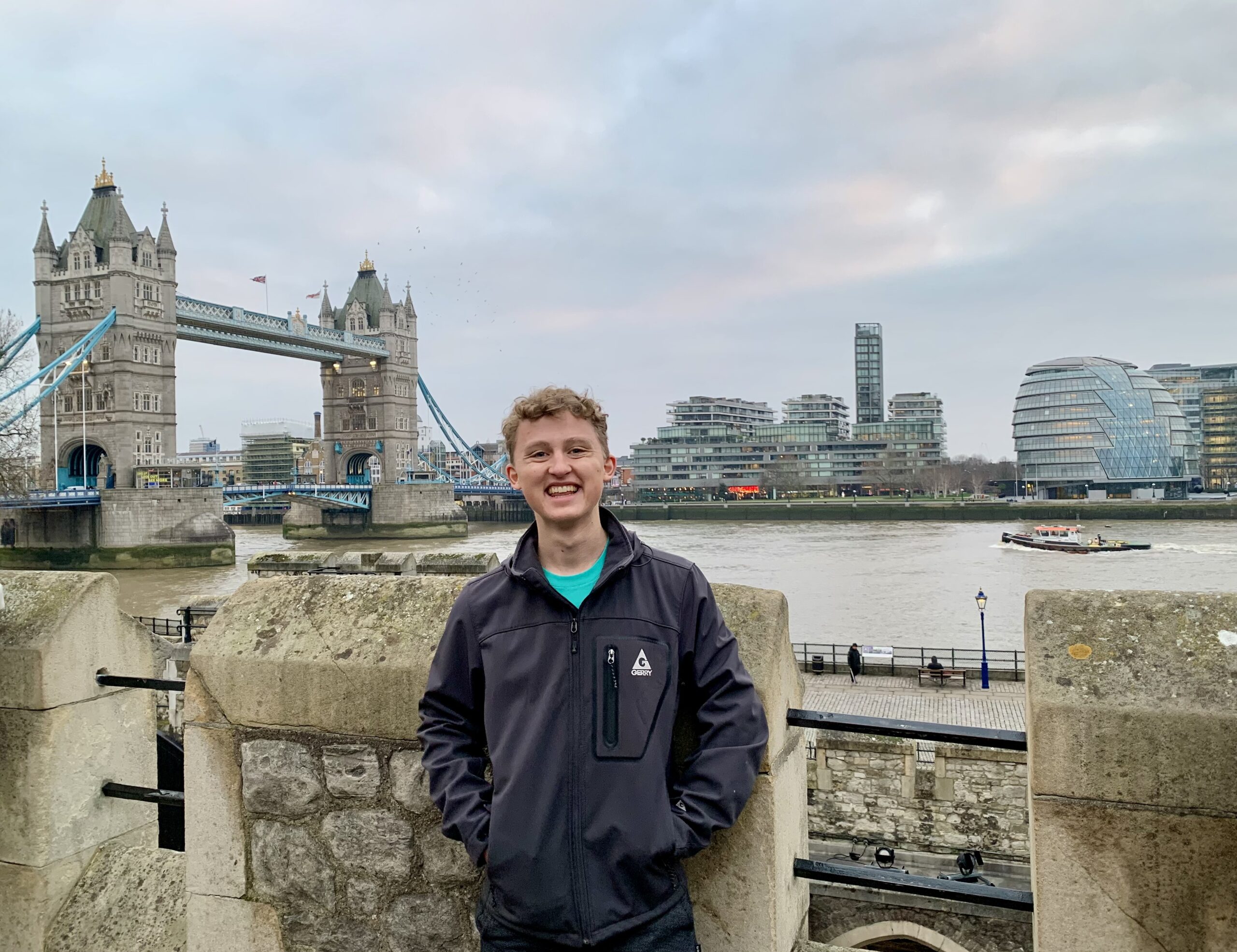 Devin smiles in front of the water with a view of Tower Bridge behind him