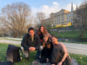 Jacki and her flatmates smile while sitting on a picnic blanket in a patch of grass