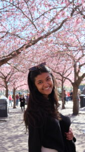 Suneri smiles in front of a tree with pink cherryblossoms