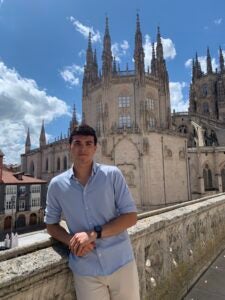 Anthony leans against the stone railing in front of Burgos cathedral on a sunny Spanish day