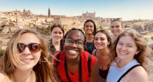 A group of students smile while the Spanish sun shines on the town and landscape behind them