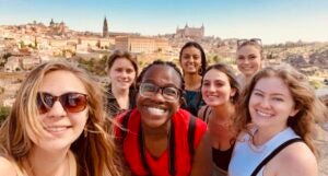 A group of students smile while the Spanish sun shines on the town and landscape behind them