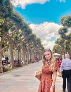 Darby Duncan poses in front of a tree-lined paved walkway in Toledo, Spain