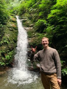 Global ambassador Jordan Matkin doing the hook 'em sign in front of a waterfall.