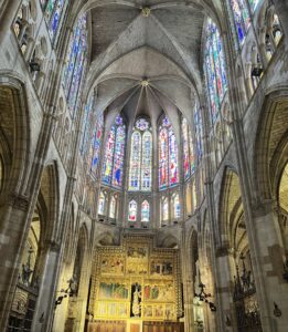 The nave of a gothic cathedral in Spain. Stained glass windows decorate the top half of the walls.