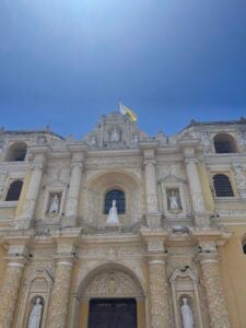 La Iglesia de Merced church is yellow with white ornamentation and trimming. A bright blue sky shines overhead.