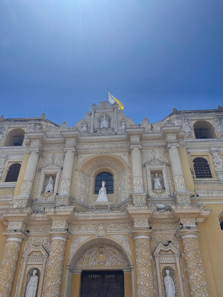 La Iglesia de Merced cathedral is yellow with white ornamentation and trimming. A bright blue sky shines overhead.