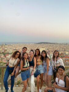 A group of women smiles against a mediterranean sea backdrop