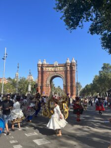 People wearing colorful traditional clothing from Bolivia walk in front of a large arch