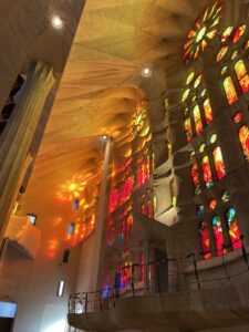A wall of stained glass at the Sagrada Familia church filters in red, orange, and yellow light from the setting sun outside
