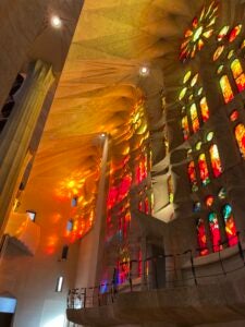 A wall of stained glass at the Sagrada Familia church filters in red, orange, and yellow light from the setting sun outside