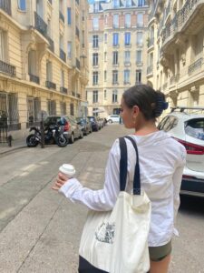 Amitai carries a tote bag and holds a cup of coffee while strolling through Parisian streets