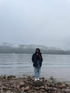 Ashley smiles while standing on top of rocks in front of a smoggy lake