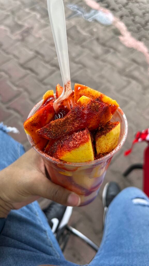 Chassity holds a cup of fruit topped with Chamoy