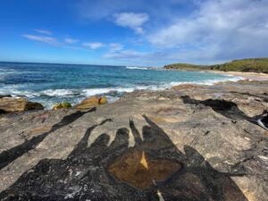 The shadows of three friends holding up the peace sign can be seen over the shore of a beach