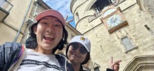 Carol and a friend take a selfie with a clock tower in the background