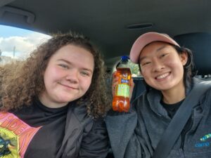 Carol and friend in a car holding a bottle of soda