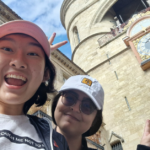 Carol and a friend take a selfie with a clock tower in the background